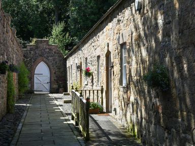 A stone pathway with a wooden railing leading to a white arched door with stone walls on both sides at Craster Tower Coach House in Craster
