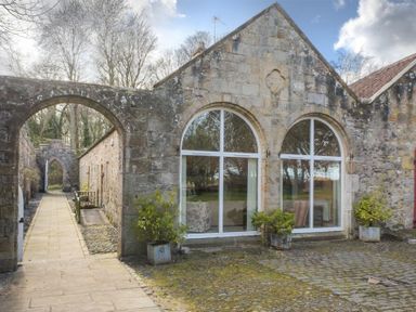 Exterior view of stone building with arched windows and archway entrance at Craster Tower Coach House in Craster