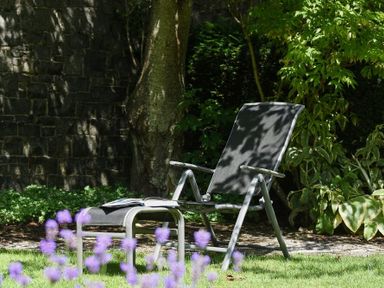 A garden with a reclining chair and footstool near a tree and stone wall at Craster Tower Coach House in Craster