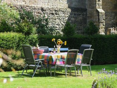 An outdoor patio table with chairs a colorful tablecloth sunflowers and a picnic basket in a garden at Craster Tower Coach House in Craster