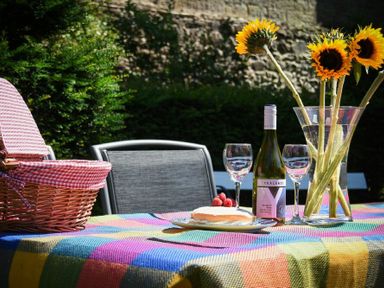 A picnic basket wine bottle two glasses cake with raspberries and sunflowers in a vase on a colorful tablecloth outdoors at Craster Tower Coach House Craster