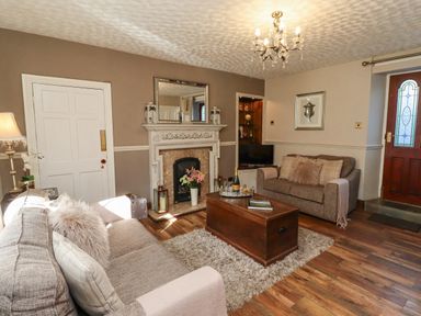 A living room with two sofas a wooden coffee table a fireplace and a wooden door at Dray Cottage in Warkworth