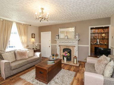 A living room with two sofas, a wooden coffee table, a fireplace with a mirror above, and a built-in shelf with decorations at Dray Cottage in Warkworth