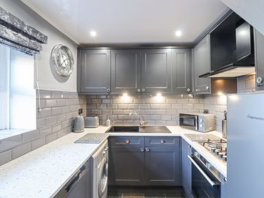 A kitchen with grey cabinets a clock on the wall and appliances at Dray Cottage in Warkworth