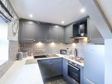 A kitchen with gray cabinets a sink a microwave stove and refrigerator at Dray Cottage in Warkworth
