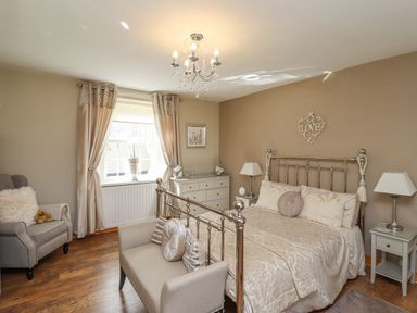 A bedroom with a metal bed frame a sofa at the foot of the bed an armchair curtains and a dresser at Dray Cottage in Warkworth