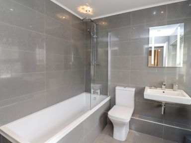 A bathroom with a bathtub shower combination toilet sink and a mirror at Dray Cottage in Warkworth