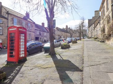 A street with parked cars stone buildings a red telephone booth and leafless trees at Dray Cottage in Warkworth