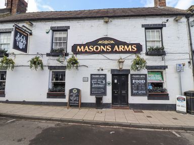 A white pub building named Masons Arms with black windows and flower boxes on a street at Dray Cottage in Warkworth