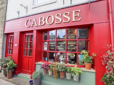 Front view of a shop named Cabosse with red doors and window frames and multiple potted plants outside the shop