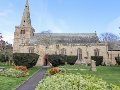 Stone church building with a clock tower and a spire surrounded by green lawn and trimmed bushes