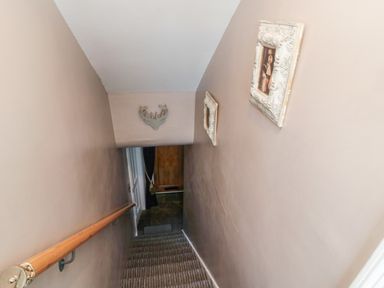A stairway with a wooden handrail leading down with framed pictures on the wall at Dray Cottage in Warkworth