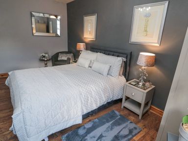 A bedroom with a bed framed by two lamps on bedside tables and artwork on the walls at Dray Cottage in Warkworth