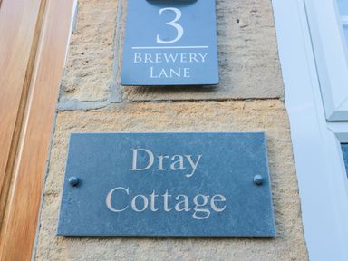 A stone wall with two signs one reading 3 brewery lane and the other reading dray cottage