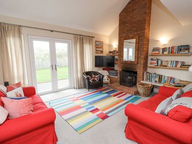A living room with red sofas a colorful striped rug a brick fireplace and bookshelves at Dunes Cottage in Beadnell