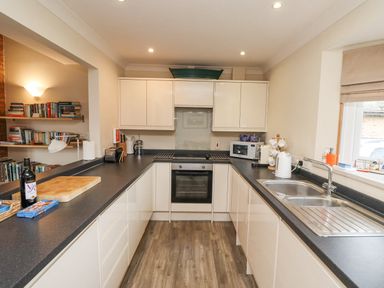 A kitchen with white cabinets black countertops a stainless steel oven and sink and shelves with books at Dunes Cottage in Beadnell