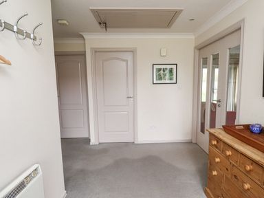 A hallway with two closed doors and a double glass door next to a wooden chest of drawers with a tray and small blue container on top at Dunes Cottage Beadnell