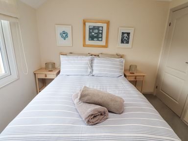 A bedroom with a bed with striped bedding and two rolled towels on it at Dunes Cottage in Beadnell