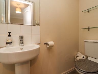 A bathroom with a sink and a mirror above it along with a toilet and a basket holding toilet paper rolls at Dunes Cottage in Beadnell