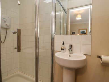 A bathroom with a shower enclosure and a pedestal sink with a mirror above at Dunes Cottage in Beadnell