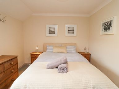 A bedroom with a bed with towels on it two bedside tables with lamps and a wooden dresser at Dunes Cottage in Beadnell
