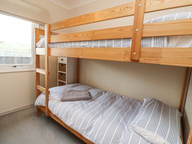 A bedroom with a wooden bunk bed and striped bedding next to a window at Dunes Cottage in Beadnell
