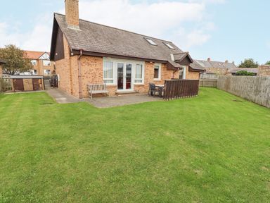 A house with a brick exterior and a fenced grassy yard at Dunes Cottage in Beadnell