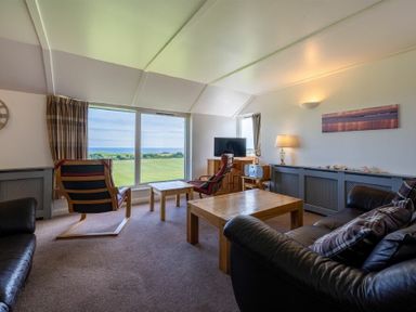 A living room with leather sofas wooden tables and chairs and a large window showing a green field and sea at Fidra in Embleton