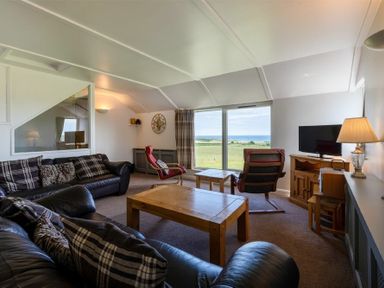 A living room with leather sofas and wooden tables facing a large window with a view at Fidra in Embleton