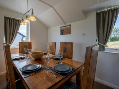 A dining room with a wooden table set with plates and glasses and two windows with curtains at Fidra in Embleton