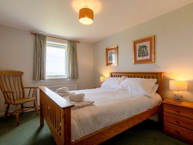A bedroom with a wooden bed with white bedding two framed pictures on the wall a wooden chair and a wooden nightstand with a lamp at Fidra in Embleton