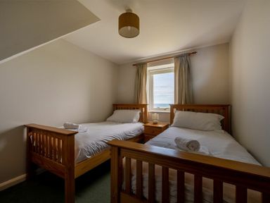 A bedroom with two single beds and a window with curtains at Fidra in Embleton