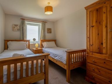 A bedroom with two single beds a wooden wardrobe a bedside table and a window with curtains at Fidra in Embleton