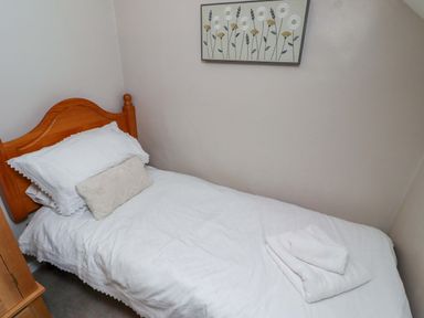 A single bed with white linens and a cushion at Heather Cottages - Grayling in Bamburgh