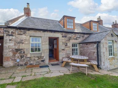 An outdoor area with a stone building and a wooden table at Heather Cottages - Grey Seal in Bamburgh