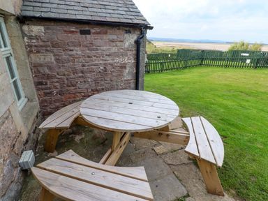 A round wooden table with benches outside at Heather Cottages - Grey Seal in Bamburgh