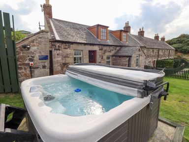 A hot tub near a stone building in the outdoor area at Heather Cottages - Grey Seal, Bamburgh