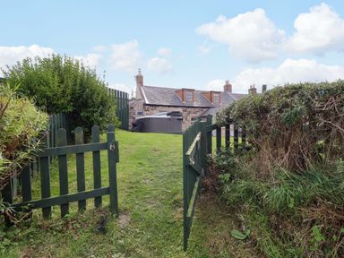A garden with a green gate and view of a house at Heather Cottages - Grey Seal Bamburgh