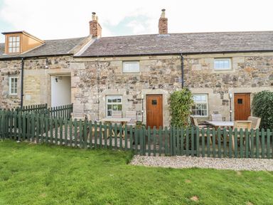 An outdoor area with a stone wall and furniture at Heather Cottages - Plover in Bamburgh