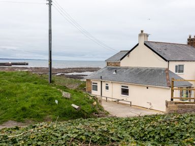 A house by the rocky shoreline with a grassy hill and power lines at Island View in Amble