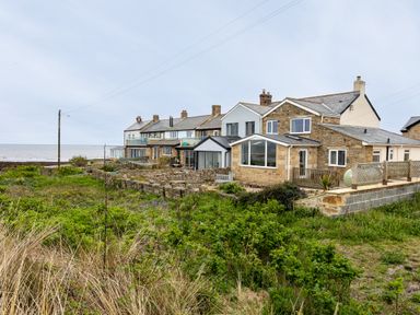 A row of stone and brick houses with glass extensions near the coast with vegetation in the foreground at Island View in Amble