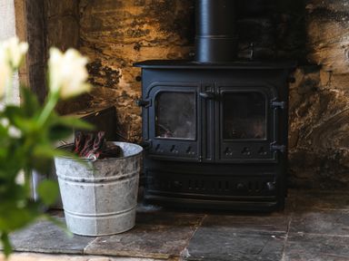 A black wood-burning stove with a metal bucket containing gloves in front at Island View in Amble