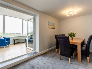 A dining area with a wooden table and black chairs next to a sitting area with a blue chair and large windows at Island View in Amble