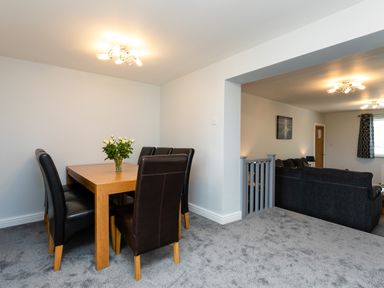 A dining area with a wooden table and six black leather chairs and a living room with gray sofas and a painting on the wall at Island View in Amble