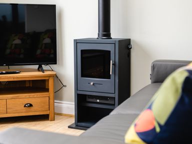 A black wood stove next to a wooden TV stand with a flat screen TV and a couch with a colorful pillow at Island View in Amble