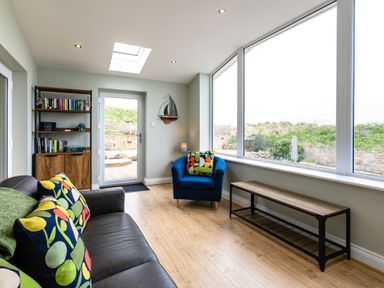 A sitting room with large windows wooden floor brown sofa blue armchair and wooden shelves at Island View in Amble