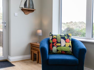 A blue armchair with a colorful patterned pillow next to a wooden side table with a lamp and a metal boat decoration on the wall at Island View in Amble