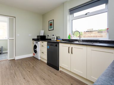 A kitchen with white cabinets a black dishwasher a washing machine a toaster a microwave a sink and a window at Island View in Amble