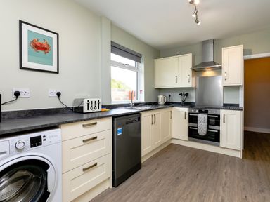 A kitchen with white cabinets a washing machine toaster dishwasher and oven at Island View in Amble