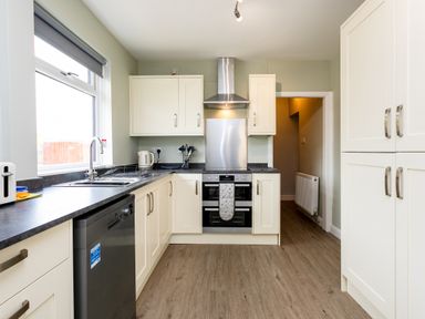 A kitchen with white cabinets black countertops a dishwasher and an oven at Island View in Amble
